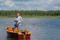 A cheerful man in yellow glasses, in a boat with oars, in the center of the lake, holds a fishing pole to catch a big fish, in the Royalty Free Stock Photo