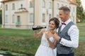 Cheerful married couple of bride in wedding dress and groom in suit pouring and drinking champagne against new house Royalty Free Stock Photo