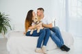 Cheerful married couple is playing with dog at home. They are sitting on sofa and stroking the animal. The man and woman are Royalty Free Stock Photo