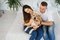 Cheerful married couple is playing with dog at home. They are sitting on sofa and stroking the animal. The man and woman are Royalty Free Stock Photo