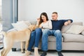 Cheerful married couple is playing with dog at home. They are sitting on sofa and stroking the animal. The man and woman are Royalty Free Stock Photo