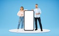 Cheerful married couple posing by big smartphone with white screen Royalty Free Stock Photo