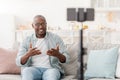 Cheerful mature african american man broadcasting from home, using smartphone and tripod, sitting on sofa at home Royalty Free Stock Photo