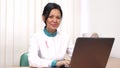 Female therapist with pink ribbon pinned to her labcoat working on the laptop