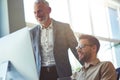 Cheerful mature businessman, male boss explaining something to young colleague, looking at PC screen and smiling while Royalty Free Stock Photo