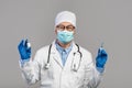 Cheerful mature chinese doctor in white coat, glasses and gloves shows vaccine and syringe