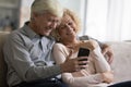 Cheerful mature elder couple using mobile phone at home Royalty Free Stock Photo