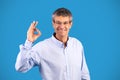 Cheerful mature European businessman showing okay sign over blue background Royalty Free Stock Photo