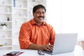 Cheerful mature indian businessman working on laptop at office Royalty Free Stock Photo