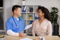 Cheerful mature korean doctor greets, congratulates with recovery black millennial lady patient in clinic