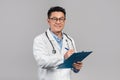 Cheerful mature korean man doctor in white coat, glasses with stethoscope writes at tablet