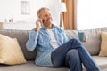Cheerful mature man talking on cellphone sitting on sofa Royalty Free Stock Photo
