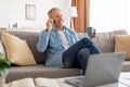 Cheerful mature man talking on cellphone sitting on sofa Royalty Free Stock Photo