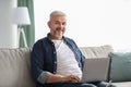 Cheerful mature man using laptop while resting on sofa Royalty Free Stock Photo