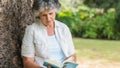 Cheerful mature woman reading book sitting on tree trunk Royalty Free Stock Photo