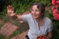 Cheerful mature woman sits in the garden and waving to friends