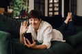 Cheerful mature woman making video call via mobile phone while lying on couch Royalty Free Stock Photo