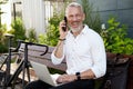 Cheerful middle aged businessman smiling, talking on the phone, using his laptop while sitting on the bench outdoors Royalty Free Stock Photo