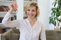 Cheerful middle aged female, real estate agent, sitting on couch, holding keys to new house Royalty Free Stock Photo