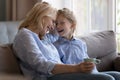 Cheerful middle-aged grandma sits on sofa with little granddaughter