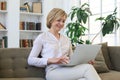 Cheerful middle aged woman using laptop while sitting on sofa at home Royalty Free Stock Photo