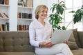 Cheerful middle aged woman using laptop while sitting on sofa at home Royalty Free Stock Photo