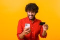 Cheerful middle eastern guy is using smartphone and credit card for shopping online. Happy man is ordering food online Royalty Free Stock Photo