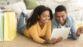 Cheerful millennial african american couple with bags with purchases lying on floor with tablet, credit card Royalty Free Stock Photo