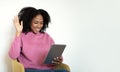 Cheerful millennial african american curly lady in casual sits on armchair, waving hand in tablet