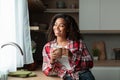 Cheerful millennial african american female with cup enjoy drink, comfort and calm, looking out window