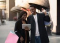 Cheerful millennial african american man in coats holds shopping bags and shows digital tablet to his wife