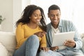 Cheerful millennial african american wife show finger at husband tablet, have video call in living room interior Royalty Free Stock Photo