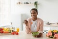 Cheerful millennial african american woman eating salad with organic vegetables in minimalist kitchen interior Royalty Free Stock Photo
