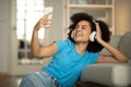 Cheerful millennial black curly lady in wireless headphones listens to music