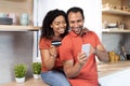 Cheerful millennial black lady hugging guy with credit card and smartphone enjoy online shopping in kitchen Royalty Free Stock Photo