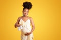 Cheerful millennial black pregnant woman touching big belly, enjoy pregnancy, show small shoes Royalty Free Stock Photo