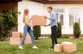 Cheerful millennial couple with cardboard boxes in front of their new house on moving day Royalty Free Stock Photo