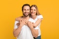 Cheerful millennial european female hugging from behind male with stubble in white t-shirts looking at camera Royalty Free Stock Photo