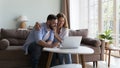 Cheerful millennial family couple using laptop in home living room