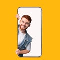 Cheerful millennial handsome european red-haired male peeks out of empty screen of big phone