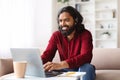 Cheerful indian man working from home, using headset and laptop Royalty Free Stock Photo