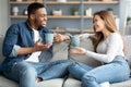 Cheerful Mixed Couple Relaxing On Couch At Home With Coffee And Chatting