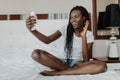 Cheerful mixed race afro american girl having video chat with friends using laptop camera while lying on bed Royalty Free Stock Photo