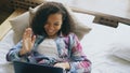 Cheerful mixed race girl having video chat with friends using laptop camera while lying on bed Royalty Free Stock Photo