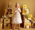 Cheerful modern little princess among 2 piles of golden gifts