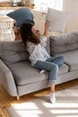 Cheerful mom and playful child playing in living room overjoyed pillow fight sitting on sofa at home