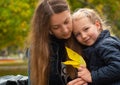 Cheerful mother and daughter smiling sitting in autumn park. Happy family walk. Cute little child playing with parent Royalty Free Stock Photo