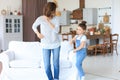 Cheerful mother with little daughter dancing at favourite song in living room at home