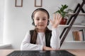 Cheerful motivated student 9 s teenager Caucasian sitting in headphones at a laptop waving hello to the laptop webcam Royalty Free Stock Photo