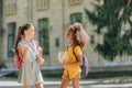 Cheerful multicultural schoolgirls holding books and talking in schoolyard